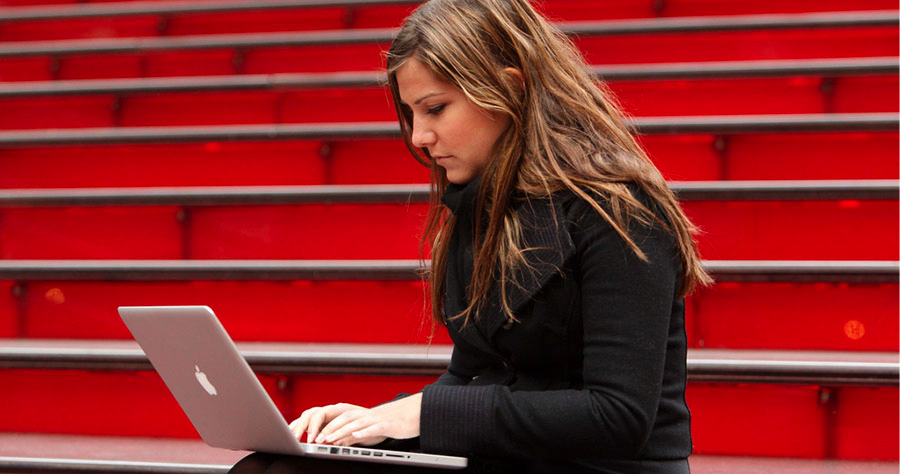 Woman using computer on red stairs.